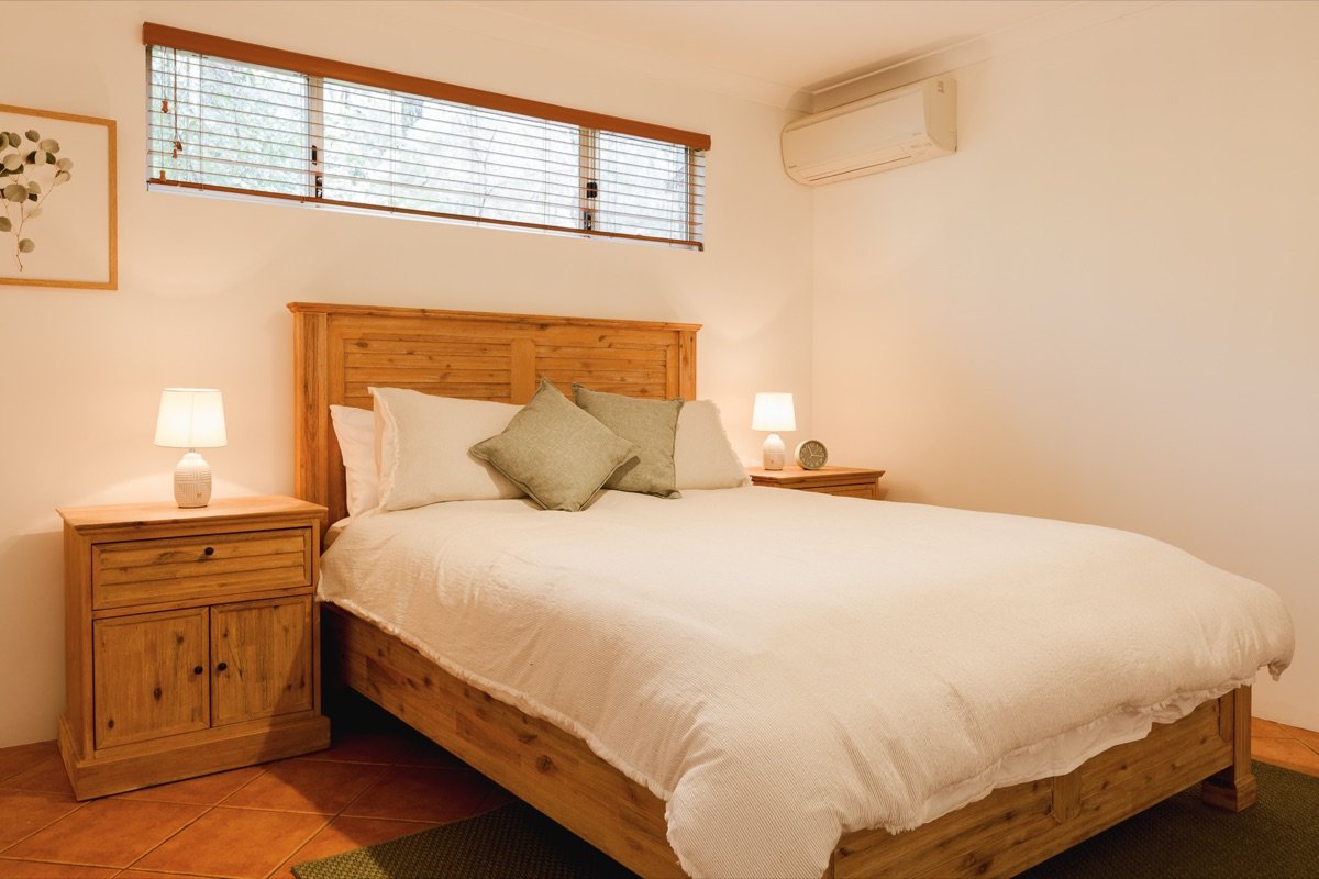 First queen bedroom with timber bed, crisp white linen and sage cushions